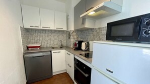 A compact kitchen with white cabinets, a black microwave, a white refrigerator, a dishwasher, and a tiled backsplash. - Port Apartment 2 Rooms Saint-Cyprien with Parking (Saint-Cyprien)