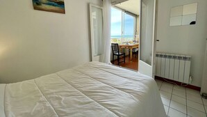 A bedroom with a bed, a painting, a view of the sea, a table with chairs, and a radiator. - Port Apartment 2 Rooms Saint-Cyprien with Parking (Saint-Cyprien)