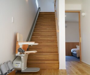 Un escalier en bois avec une rampe, une chaise et une petite table équipée d’un panneau de commande.