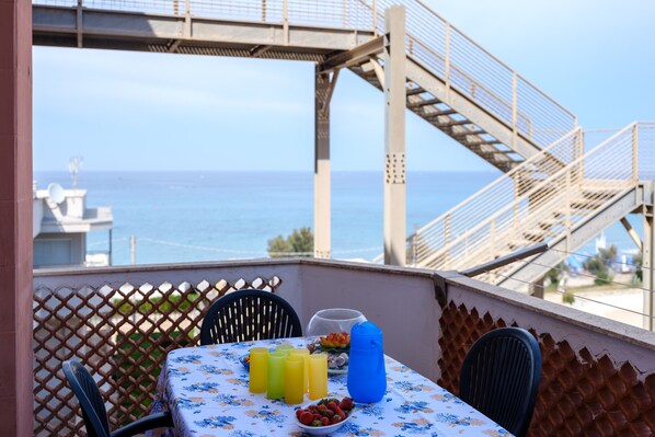 Un balcón con una mesa preparada para dos personas, una jarrón azul de agua y un cuenco de fruta.