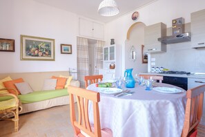 A dining area with a table set for two, a sofa, and a kitchen in the background.