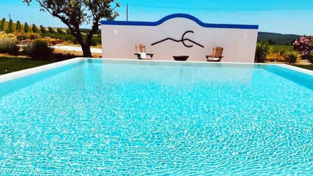 A clear swimming pool with a hat on the edge, a lounge chair, and a wall with a wave design.