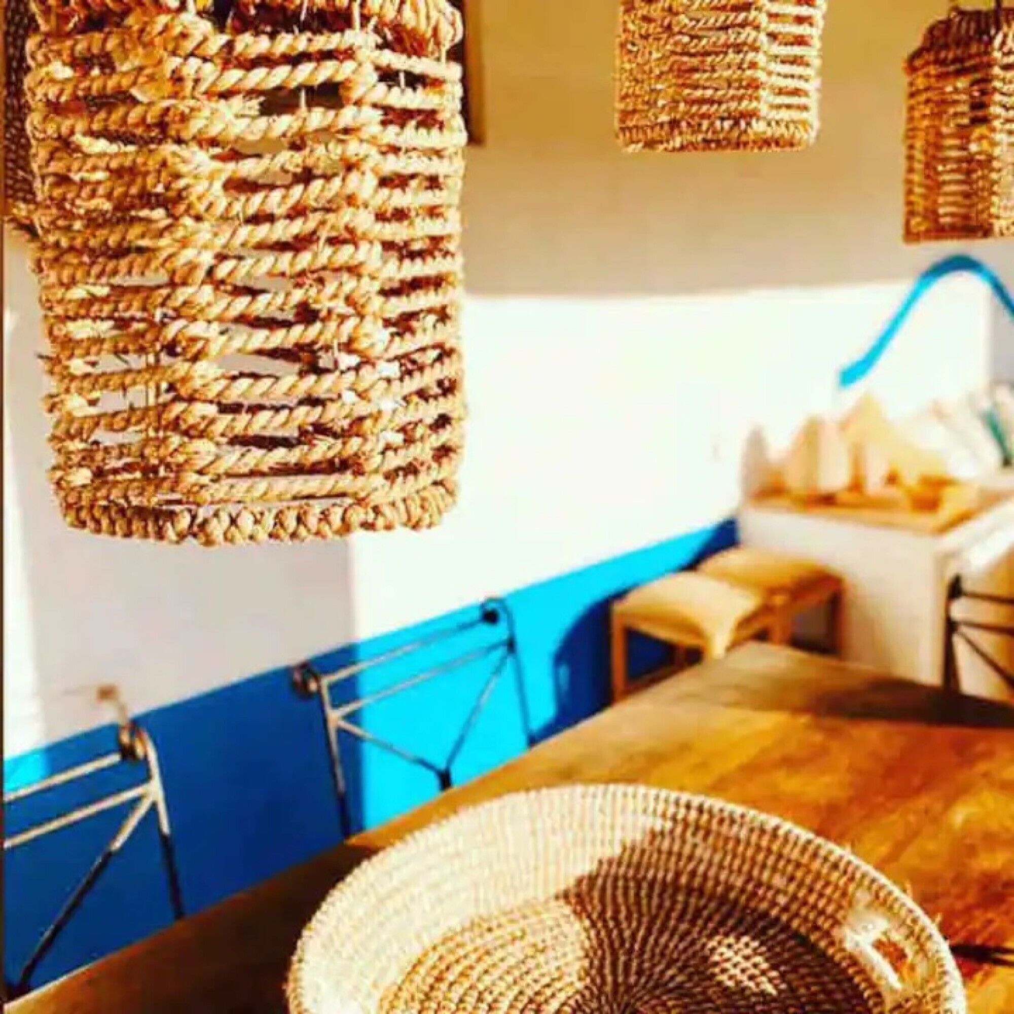 Un comedor con una mesa de madera, lámparas colgantes de mimbre y una pared azul de acento.