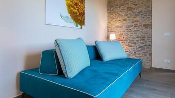 Un sofá cama color turquesa con almohadas a juego, una pared de piedra y un cuadro de una flor en la pared.