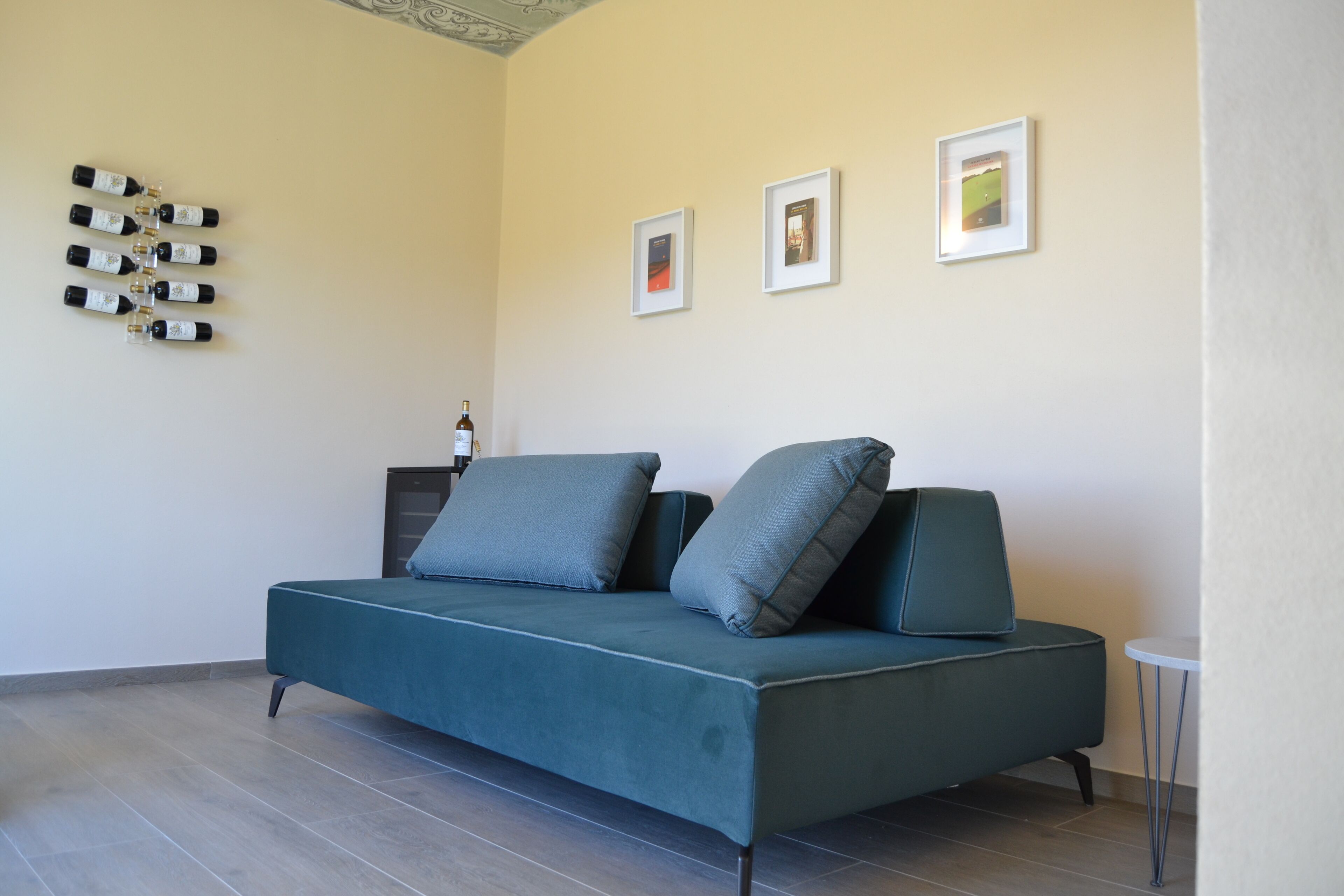 Een moderne woonkamer met een blauwgroene bank, een klein rond tafeltje en een wandrek voor wijn.