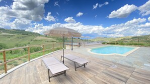 Un espace aménagé au bord de la piscine, avec une terrasse en bois, des chaises longues et une vue sur la campagne.