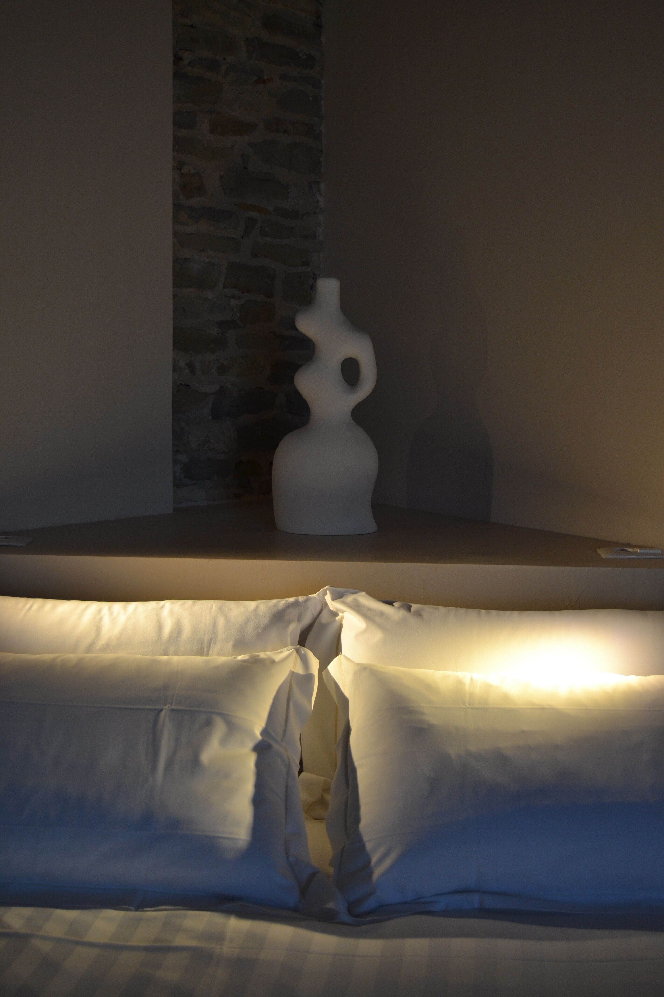Een bed met wit beddengoed en een witte vaas op een nachtkastje.