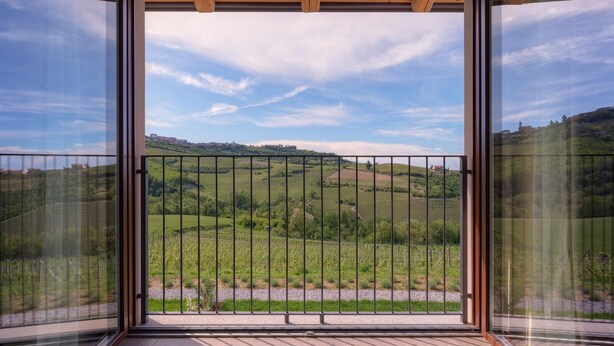 Un balcon doté d’une balustrade en métal, donnant sur un paysage verdoyant avec des collines et un ciel dégagé.