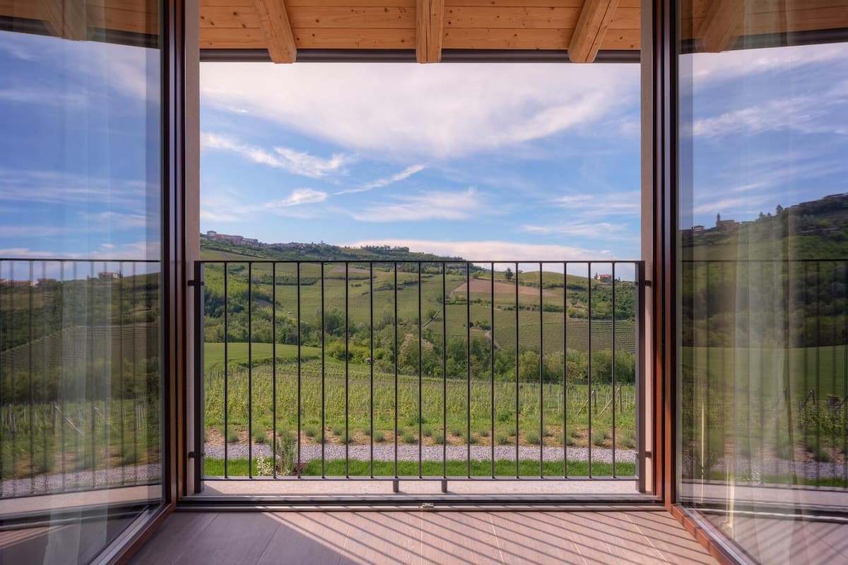 A balcony with a metal railing overlooking a green landscape with hills and a clear sky.