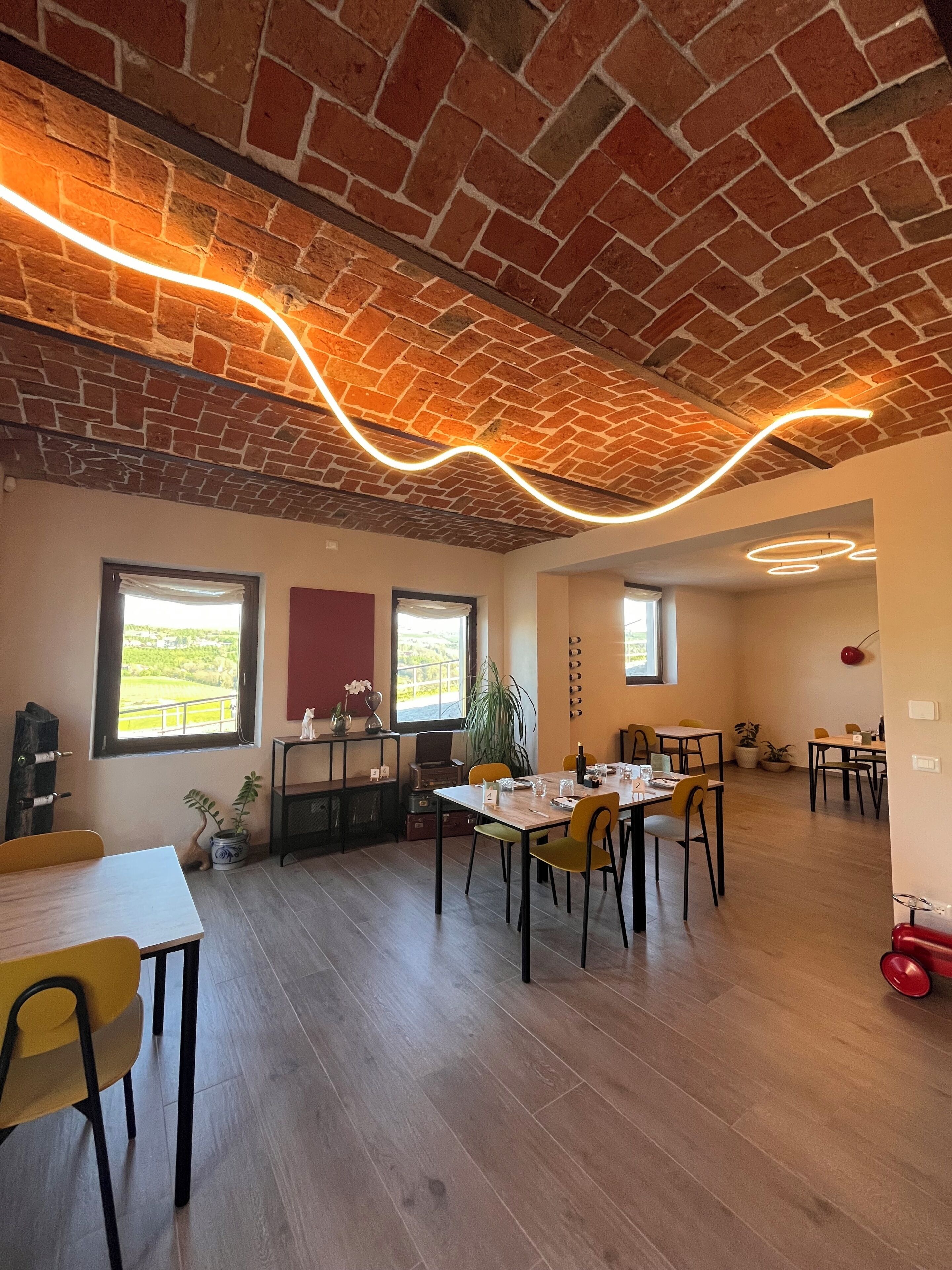Un espace repas avec un plafond en briques, des tables en bois, des chaises jaunes et de grandes fenêtres offrant une vue dégagée.