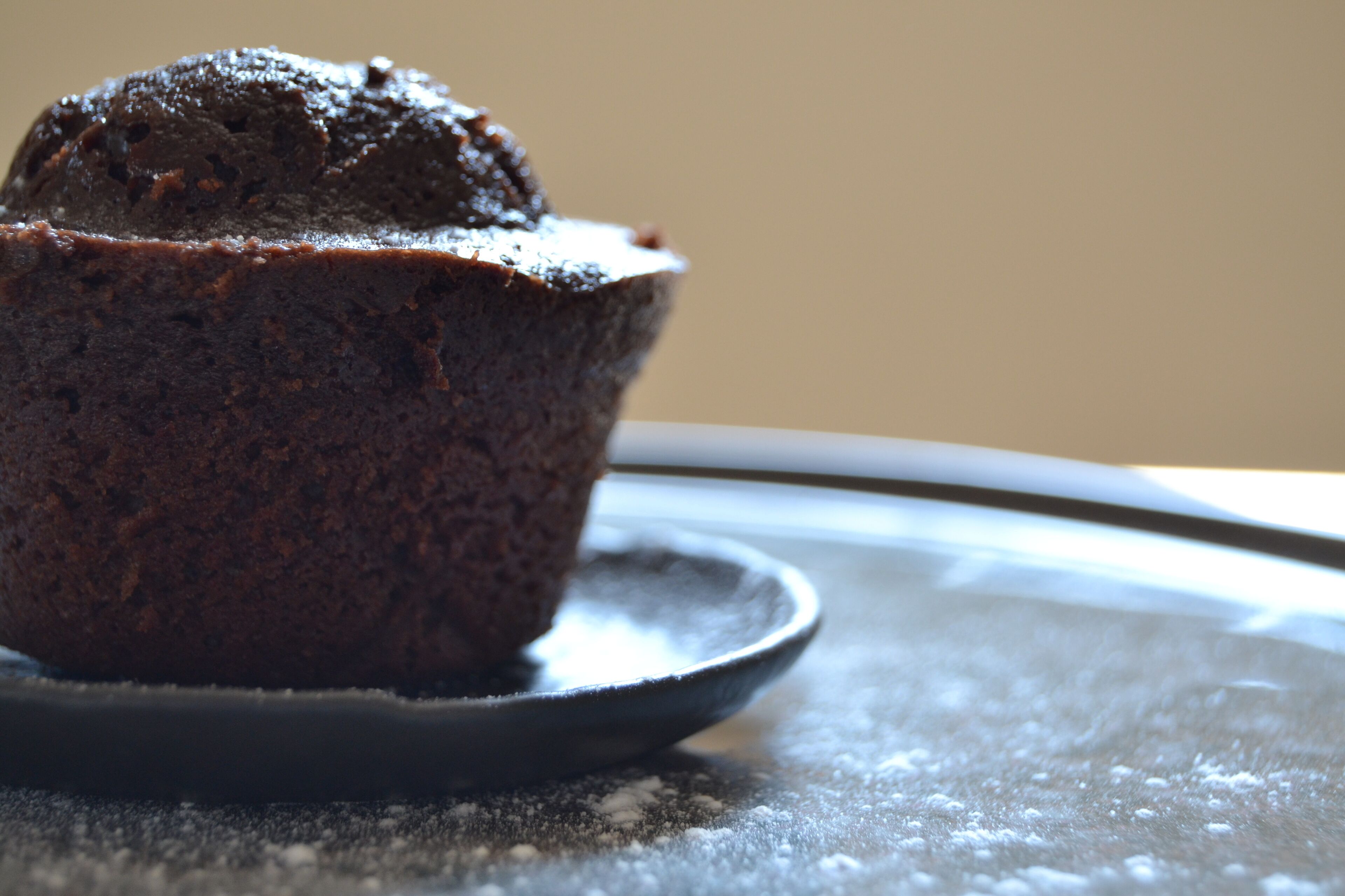 Un muffin au chocolat sur une assiette, recouvert d’une fine couche de poudre à sa surface.