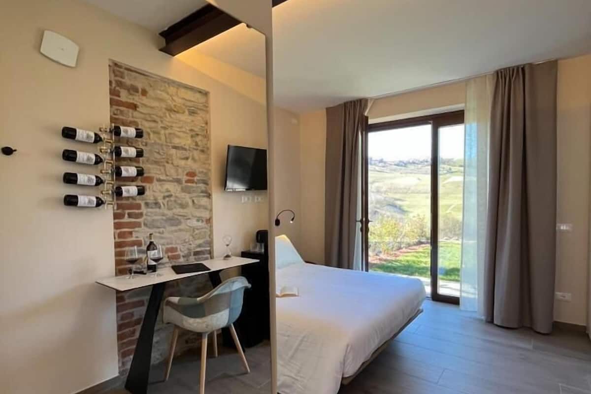 A modern hotel room with a bed, desk, and a stone accent wall.