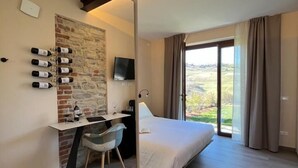 Une chambre d’hôtel moderne comprenant un lit, un bureau avec une chaise, un téléviseur à écran plat, un mur décoratif en pierre et une grande fenêtre avec des rideaux.