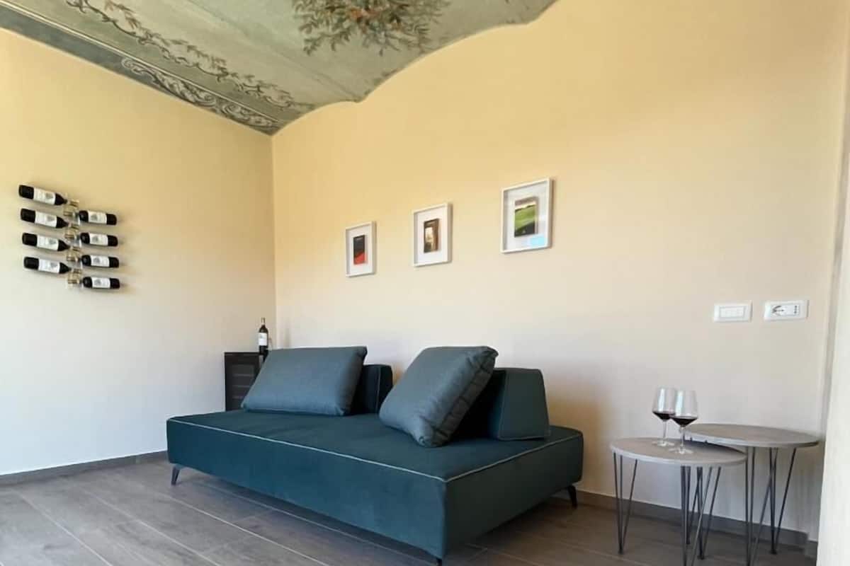 A modern living room with a teal sofa, a small round table with two wine glasses, and a decorative ceiling.