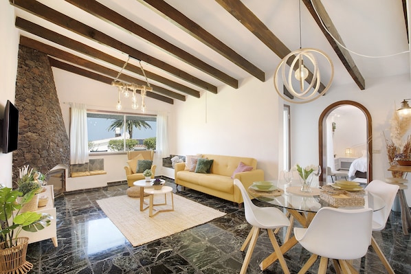 A modern living room with a sofa, dining table, and chairs, a stone accent wall, and a large window with a view.