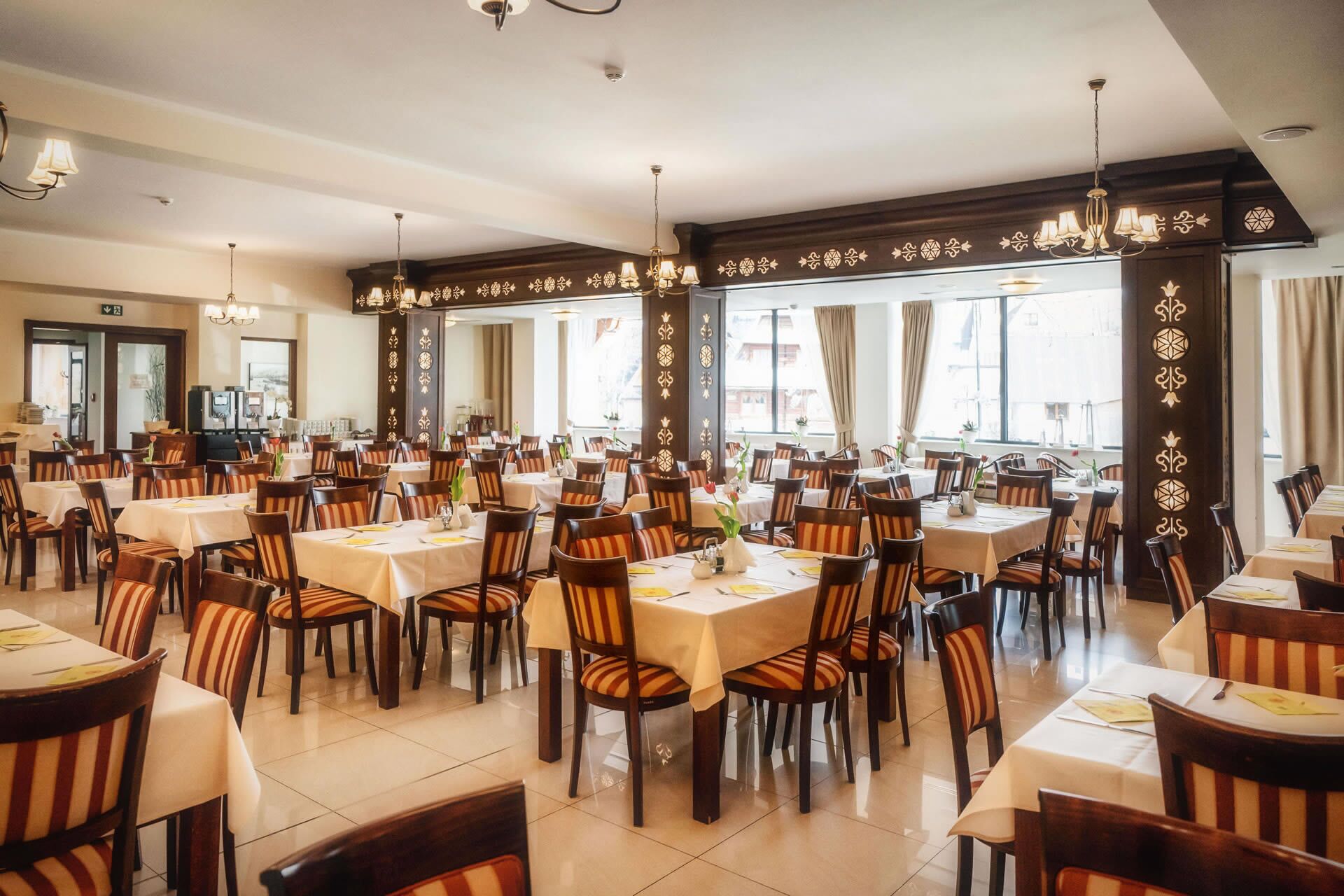 A spacious dining area with multiple tables and chairs, large windows, and decorative wall panels.
