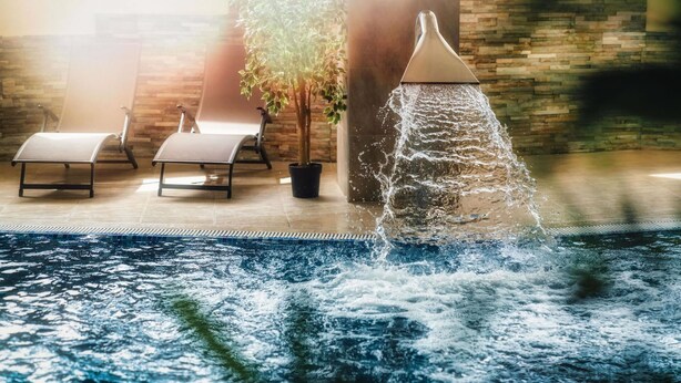 Zona de piscina con fuente, sillones de descanso y pared de piedra.