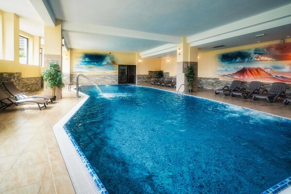 An indoor swimming pool with clear blue water, surrounded by lounge chairs and a mural depicting a mountainous landscape. - Hotel Tatra (Zakopane)