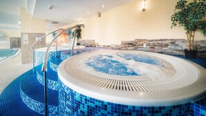 Un jacuzzi con suelo de baldosas, pared de piedra y una planta en maceta.