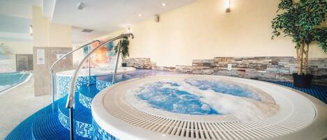 A hot tub with a tiled floor, a stone wall, and a potted plant.