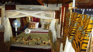 A room with a bed under a mosquito net, a fan, and patterned curtains. - Zikomo Safari Lodge (South Luangwa National Park)