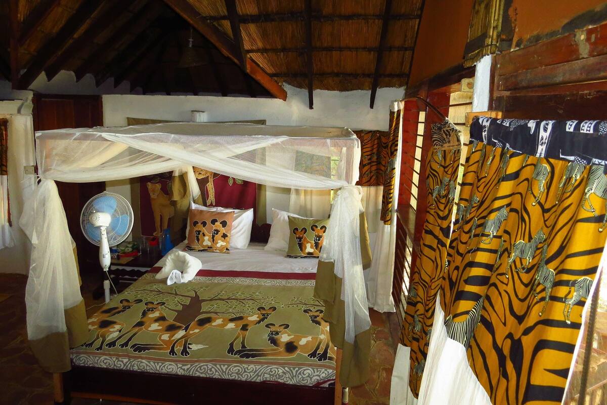 A room with a bed under a mosquito net, a fan, and patterned curtains.