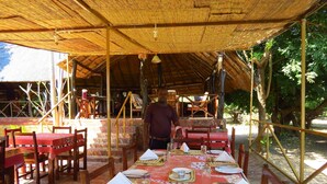 An outdoor dining area with tables set for meals, covered by a thatched roof. - Zikomo Safari Lodge (South Luangwa National Park)