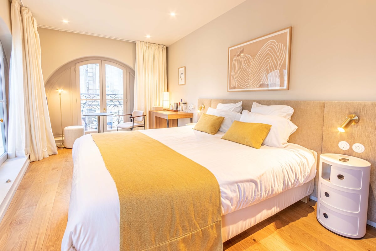 Une chambre d’hôtel avec un grand lit, une table de chevet, une lampe et une vue sur l’extérieur.