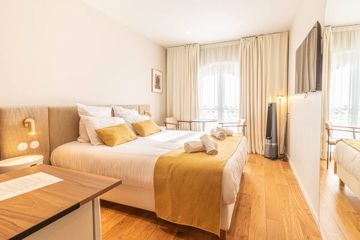 Une chambre d’hôtel avec un grand lit, des tables de chevet, un bureau, un téléviseur à écran plat et une fenêtre avec des rideaux.