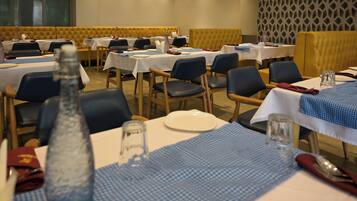 Un restaurant où les tables sont dressées pour le service, avec un mélange de nappes blanches et bleues, et un mur à motifs en arrière-plan.