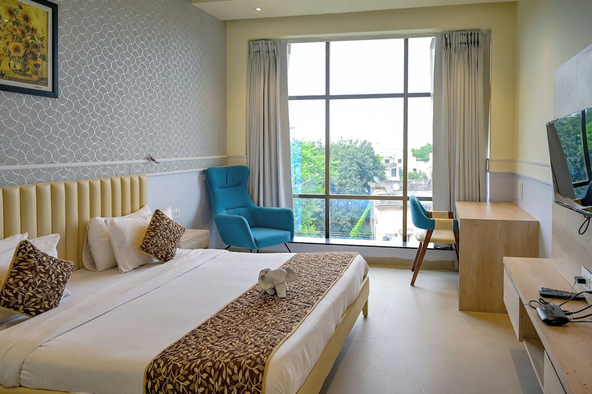 A hotel room with a large bed, a blue chair, a wooden desk, and a TV.
