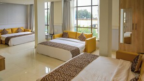 Habitación de hotel con dos camas, un sofá, un espejo y ventanas amplias.