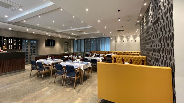 Un restaurante con mesas preparadas para comer, una zona de bar y una sección de asientos con sofás acolchados amarillos.