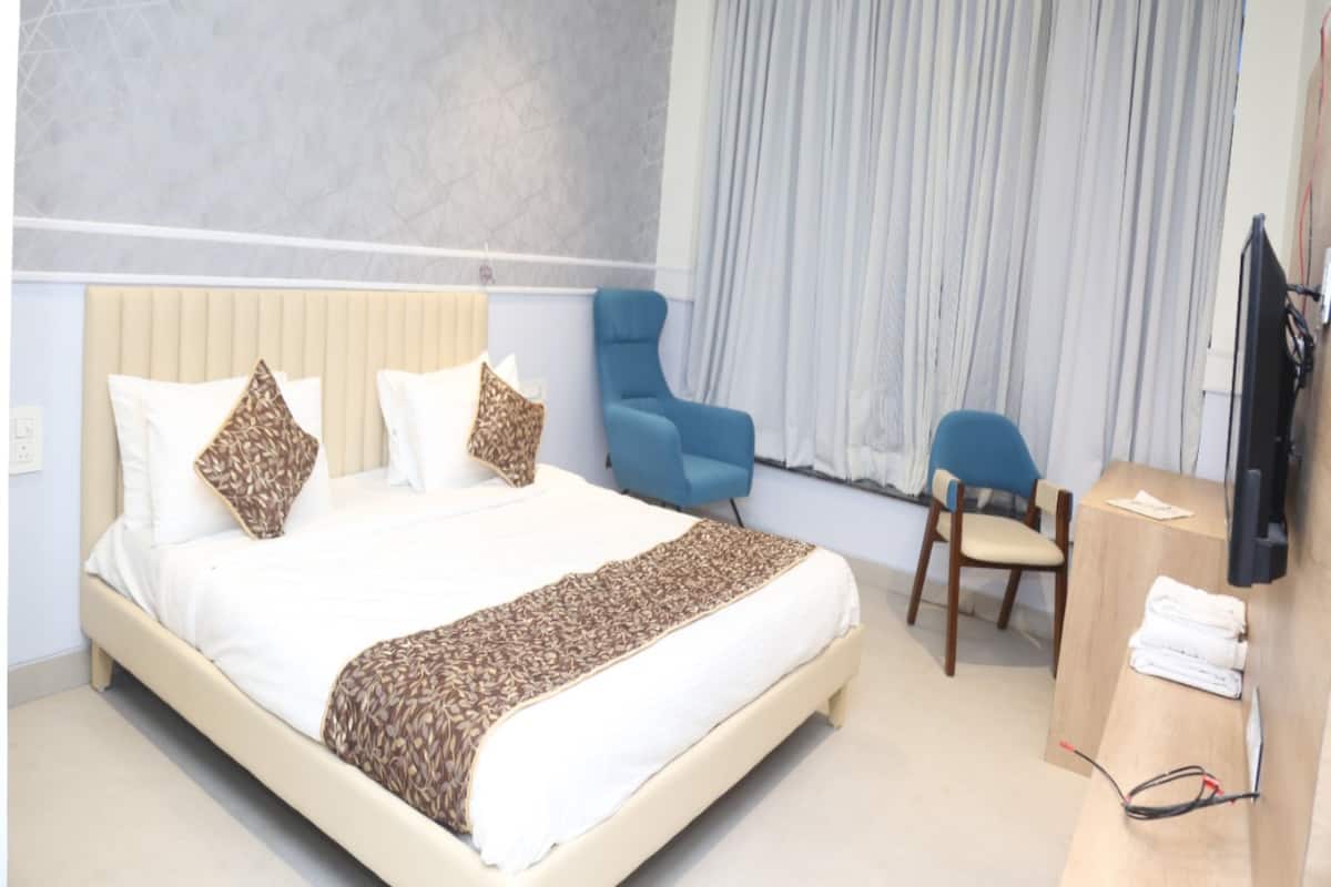 A hotel room with a bed, two chairs, a desk, and a television.
