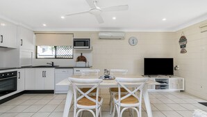 A modern kitchen with white cabinetry, a dining area with a table and chairs, a ceiling fan, and a flat-screen TV. - Iluka Villa 10 right on the Clarence River (ILUKA)