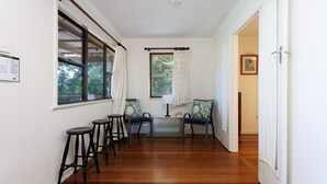 A hallway with wooden flooring, a dining table with chairs, and a window with curtains. - Serenity Now Great Location (Iluka)