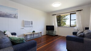 A living room with two sofas, a TV on a stand, a small table, and a window with curtains. - Serenity Now Great Location (Iluka)