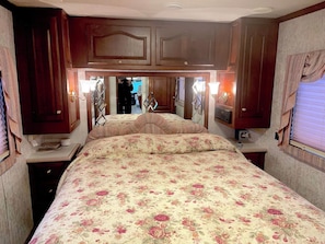 Een slaapkamer met een groot bed, houten kastjes en een spiegel boven het bed.