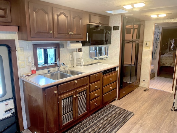 A compact kitchen with wooden cabinets, a microwave, a coffee maker, and a dishwasher.