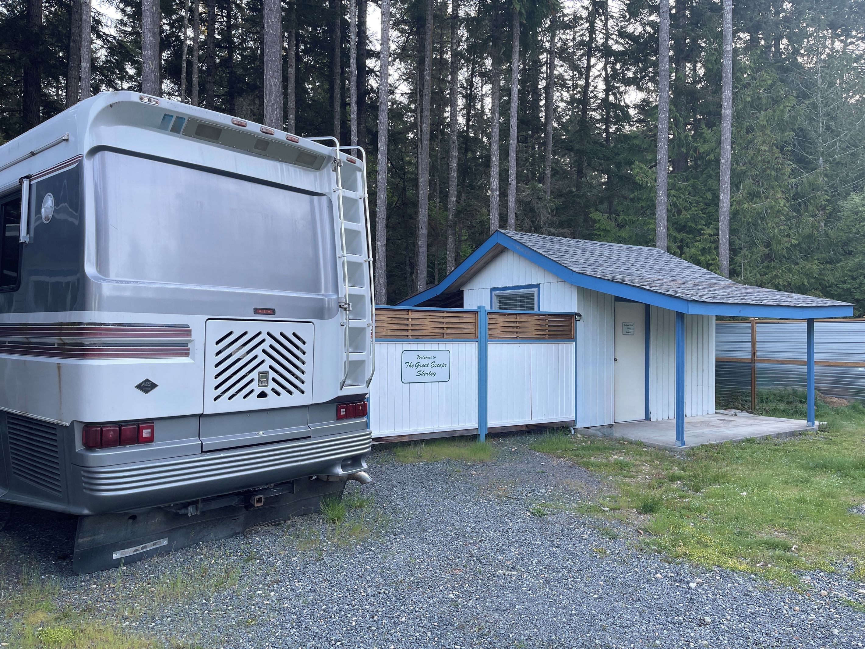 Una furgoneta camper estacionada junto a un edificio pequeño con un letrero que dice 'Welcome to The Great Escape Shady'.