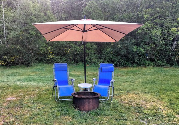 Un espace extérieur aménagé avec deux chaises bleues et une table placés sous un grand parasol.
