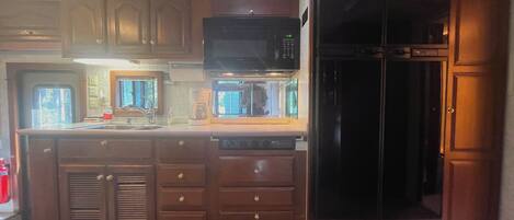Una cocina con armarios de madera, microondas, refrigerador y cafetera.