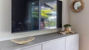 A modern living room with a large flat-screen TV mounted on the wall, a white cabinet below, and a decorative plant on the cabinet. - Mali Apartments with balcony and nice views (Tirolo)