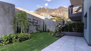 Un edificio moderno con balcón, un jardín cuidado y una vista de las montañas al fondo.