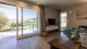 Una sala de estar moderna con un amplio ventanal corredizo que da a un patio, una mesa de centro de madera, un sofá y un televisor de pantalla plana montado en la pared.