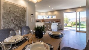Un comedor con una mesa preparada para cuatro personas, una planta en maceta y vistas a la cocina y al patio exterior.
