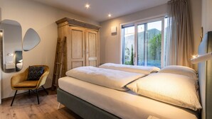 Un dormitorio con dos camas, un armario, una silla y un ventanal con vistas a zonas verdes.