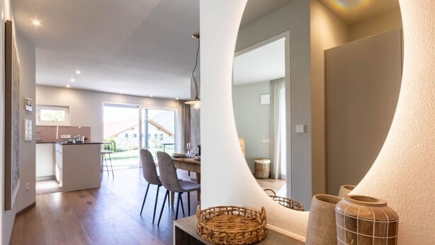 Una cocina moderna con una isla central, comedor con sillas y vistas al exterior.