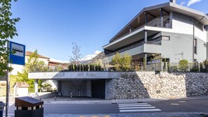 A modern building with a stone facade, a covered entrance, and a pedestrian crossing. - Mali Appartments Lounge (Tirolo)