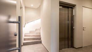 A modern interior with a staircase leading to an elevator, a door with a handle, and a light fixture above the stairs. - Mali Appartments Lounge (Tirolo)